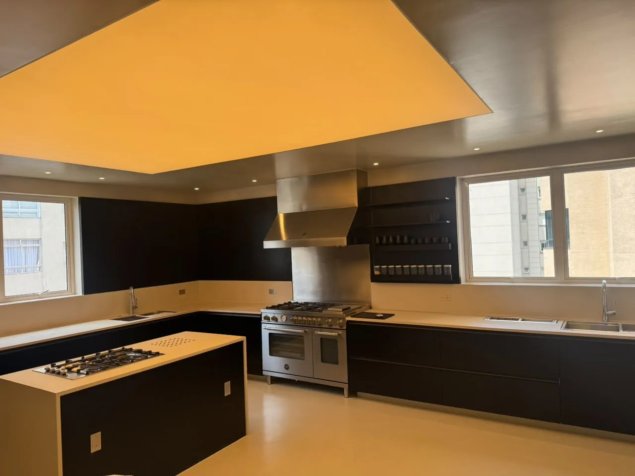 Cozinha com forro iluminado, ilha com cooktop, fogão e coifa de inox