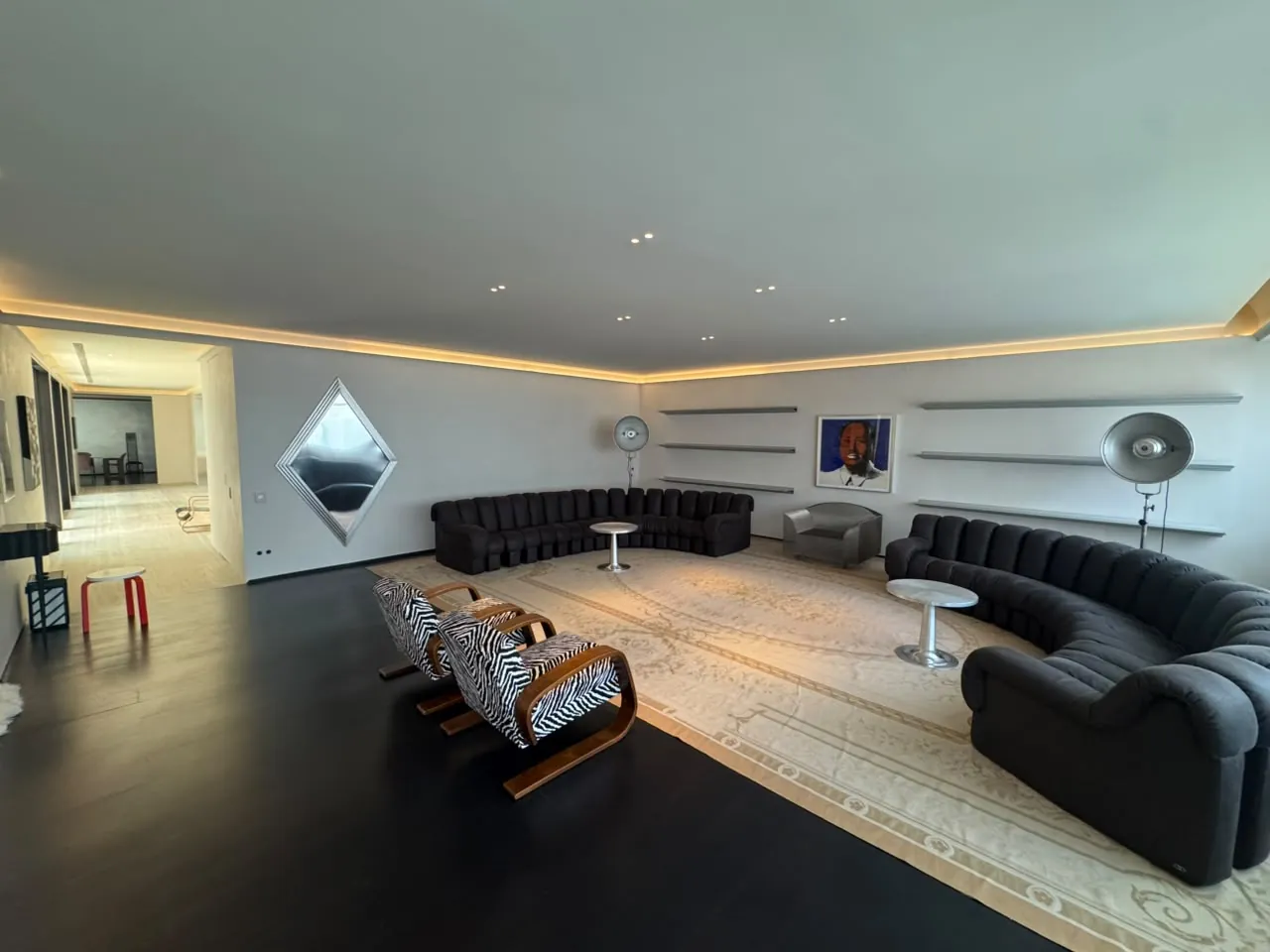 Living de apartamento com sofás pretos, tapete claro, sanca de LED e spots no forro
