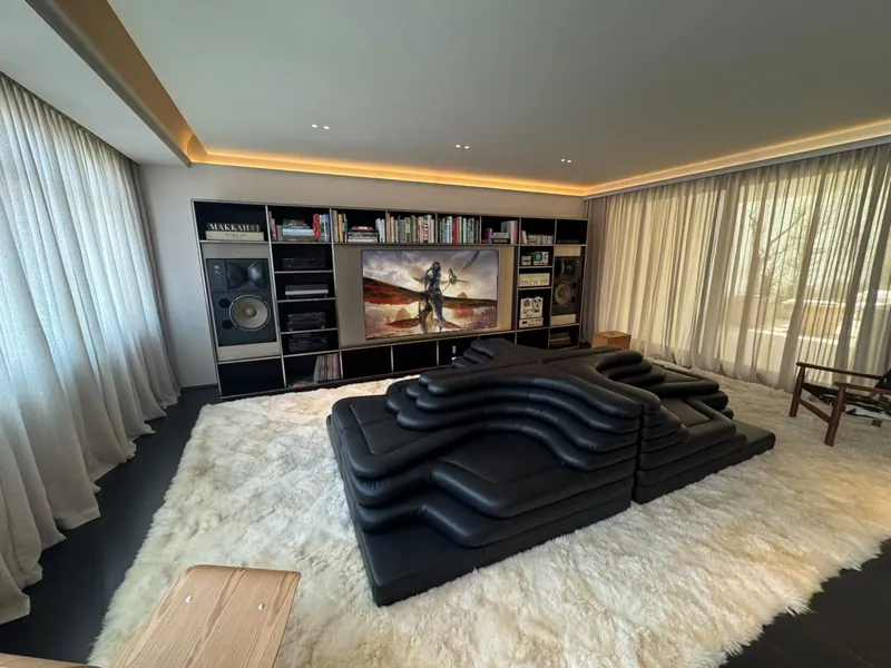 Sala de TV com estante de livros, caixas acústicas, sofá preto em degraus e filme na TV