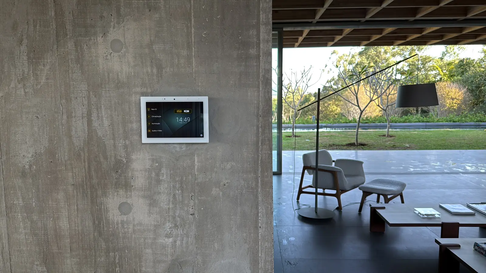 Automation touch panel on a concrete wall, with the terrace and garden behind it