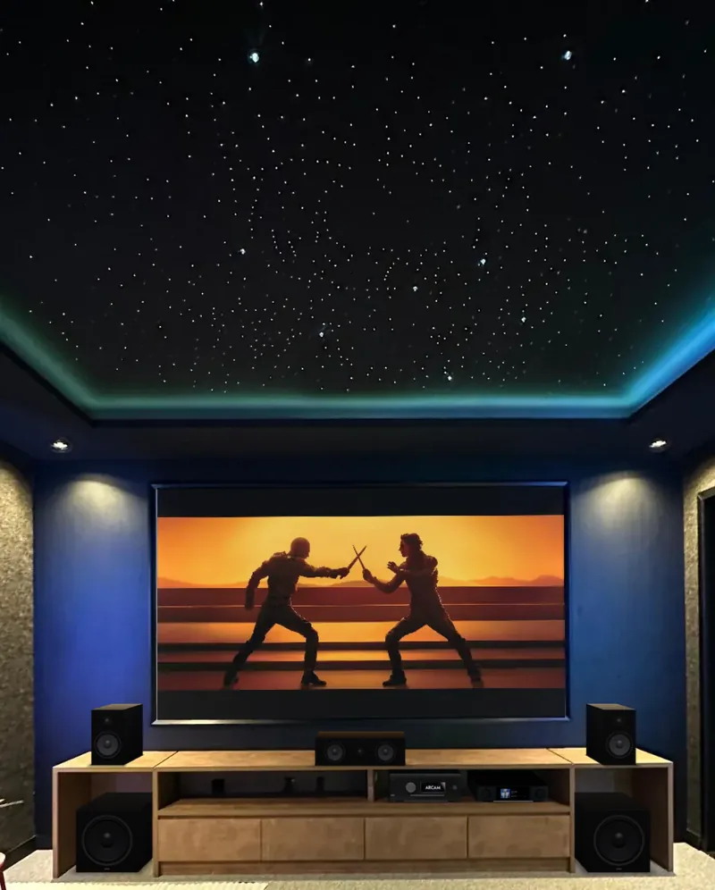 Cinema com teto estrelado, filme na tela, caixas acústicas e subwoofers na estante