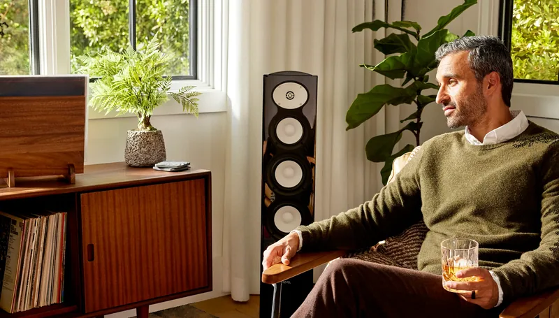 Pessoa ouvindo música na sala, ao lado de uma caixa acústica Revel