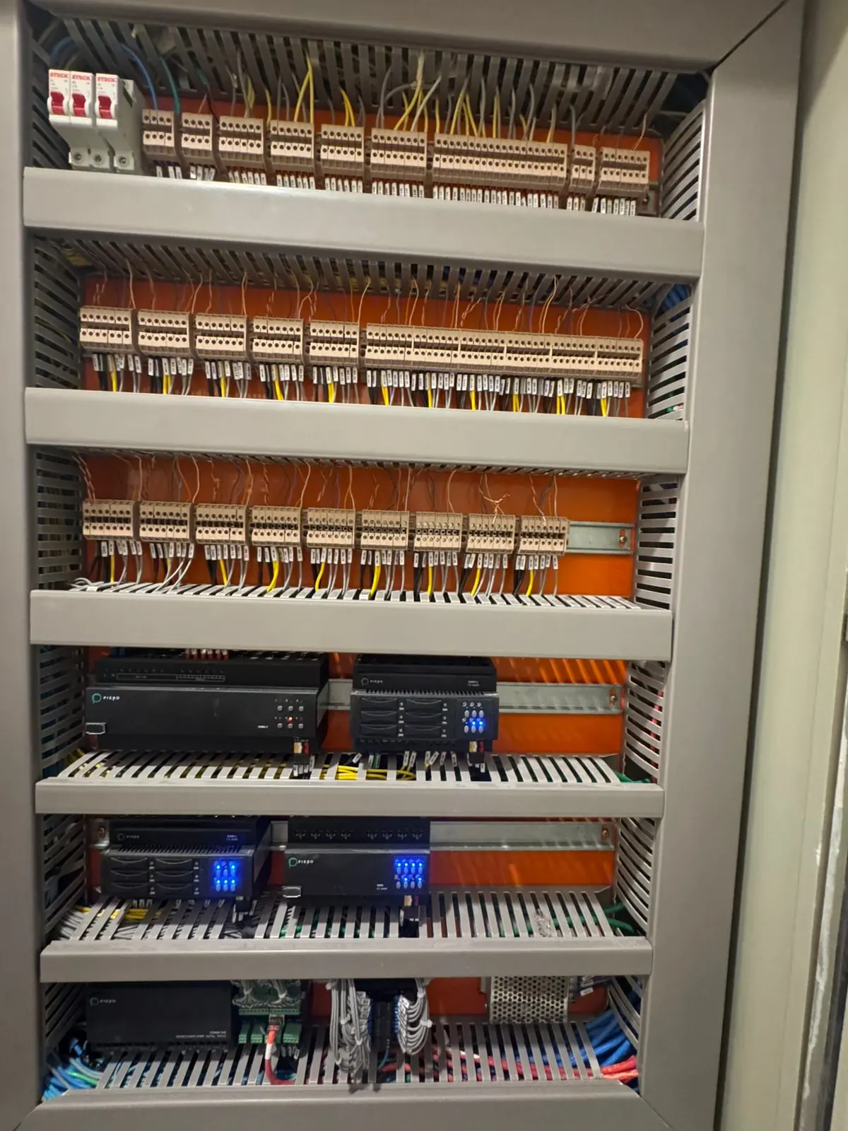 Quadro de automação organizado, com módulos, bornes identificados e fundo laranja
