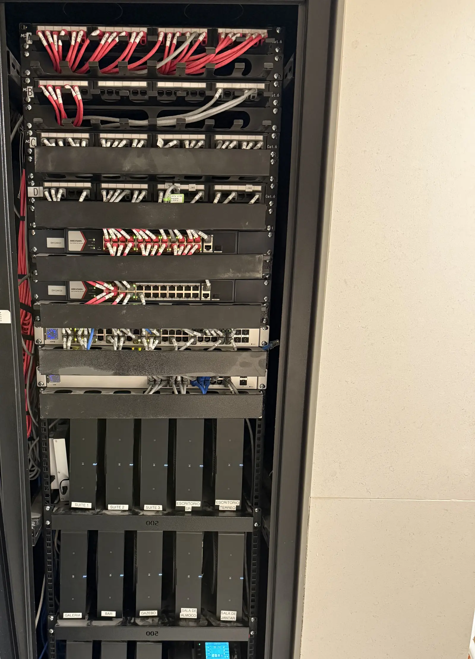 Rack de rede alto com patch panels, switches e cabos identificados