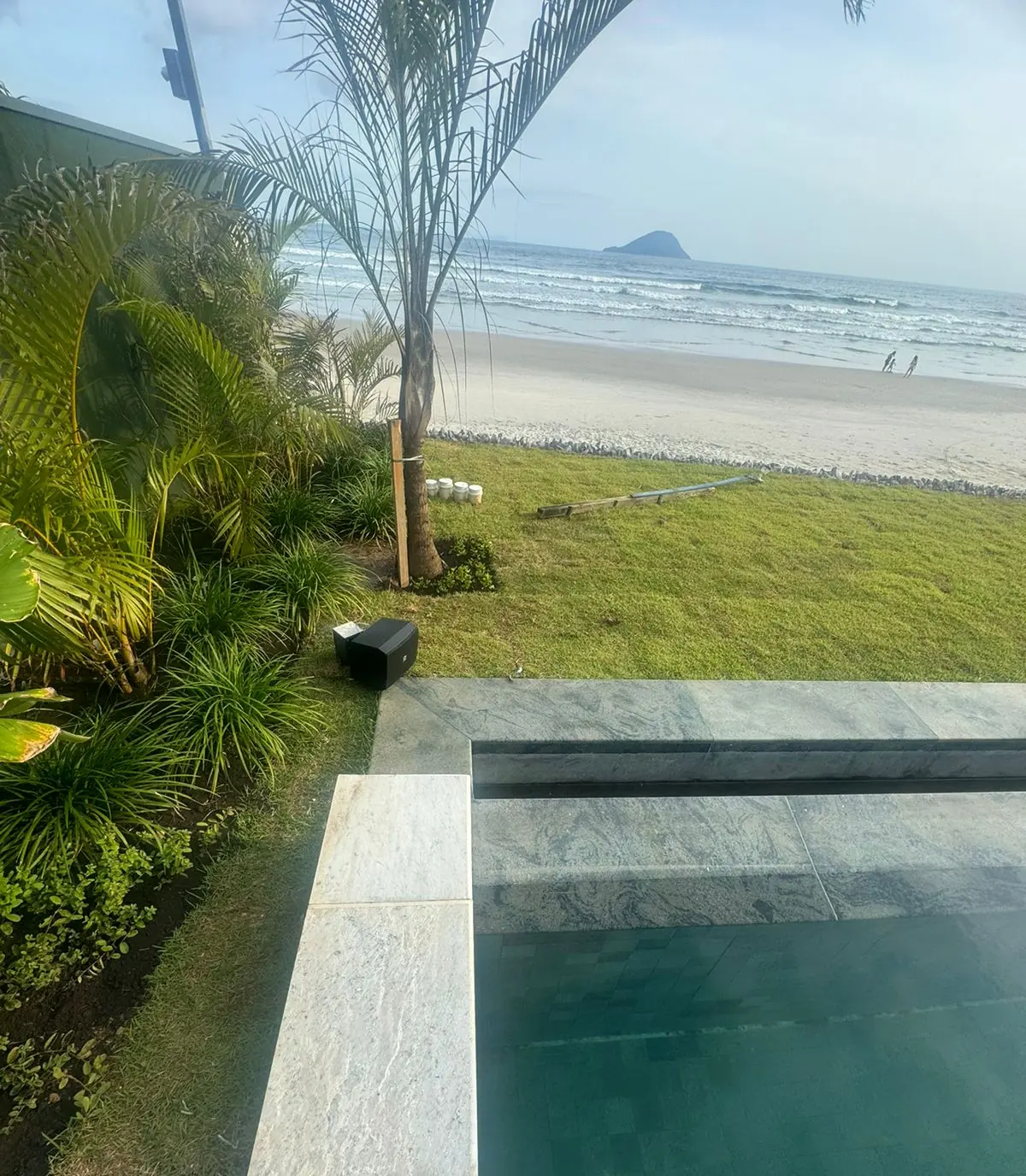 Jardim e piscina de casa de praia com caixa de som externa e o mar ao fundo