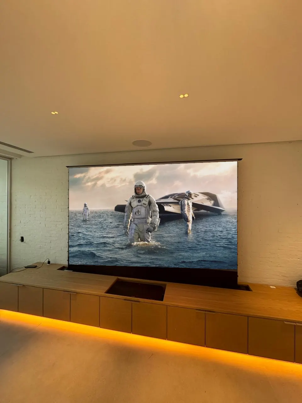 Tela de projeção que sobe do móvel da sala, com filme na tela e LED âmbar no rodapé